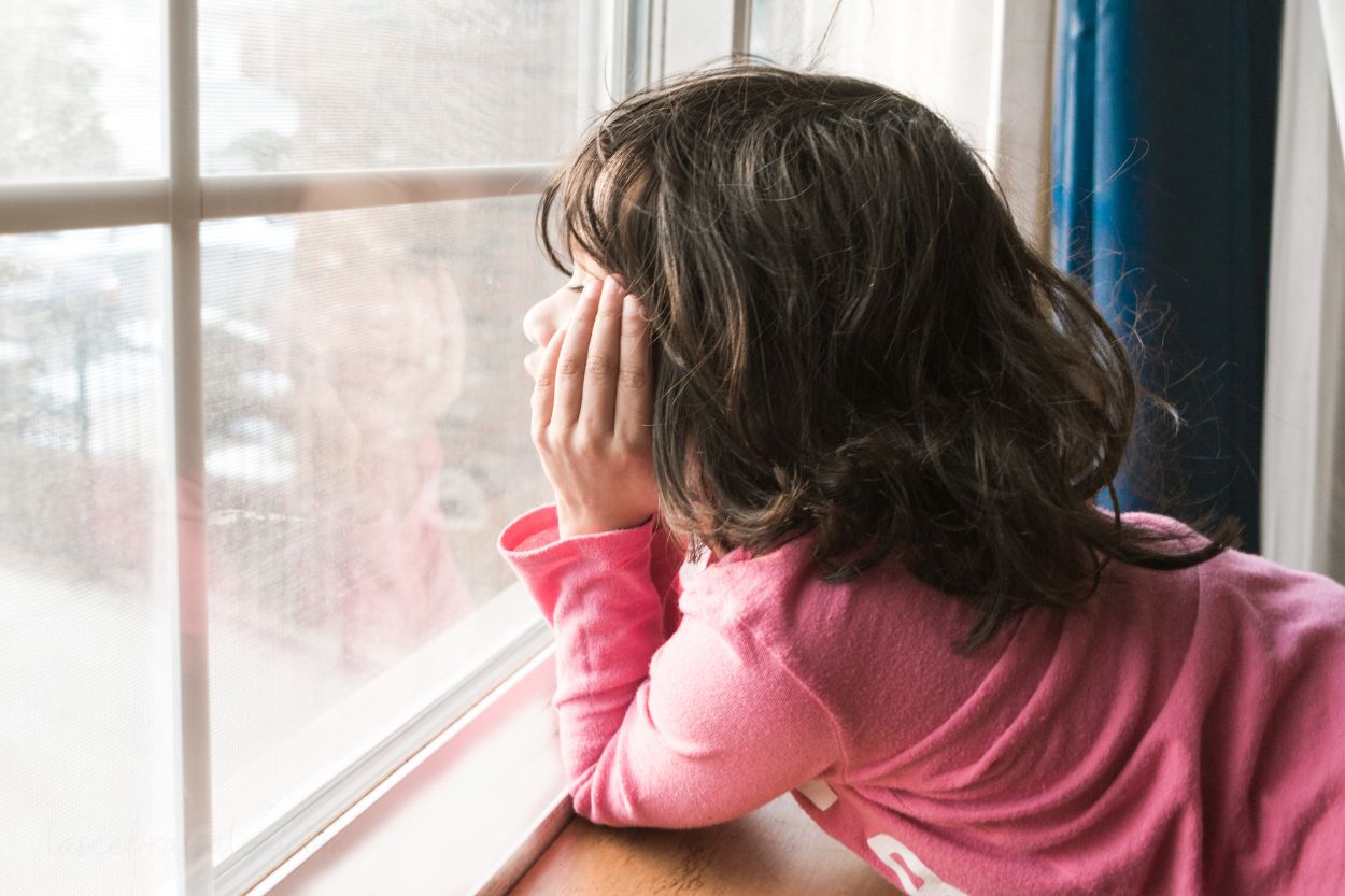 Niña pequeña mirando por la ventana con gesto curioso, una posible señal de altas capacidades