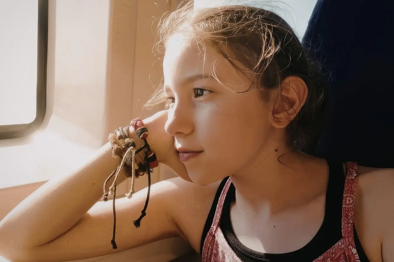 Niña mirando por la ventana mientras reflexiona sobre sus emociones y la comunicación asertiva