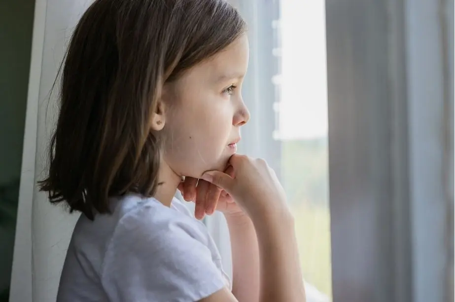 Niña mirando por la ventana mientras reflexiona en silencio sobre sus emociones