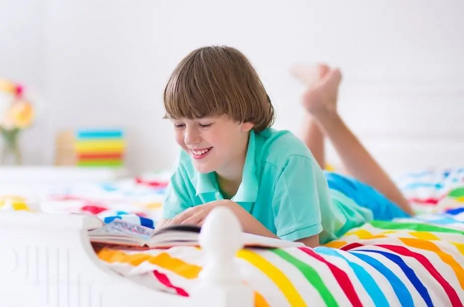 niño sonriendo mientras lee un libro infantil en su cama