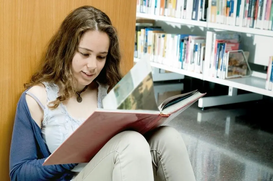 Adolescente leyendo un libro en una biblioteca