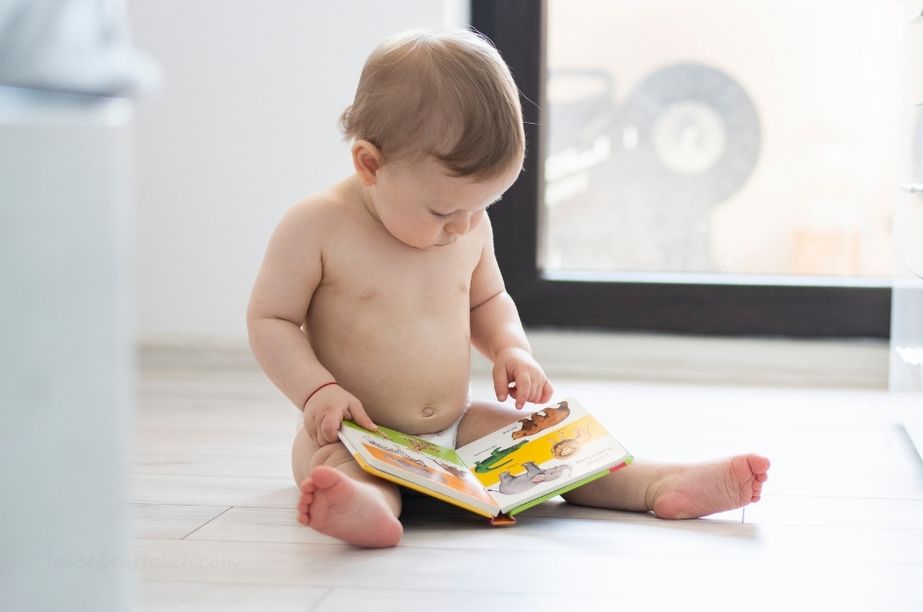 bebé mirando libro de cartón y señalando imágenes a partir de 12 meses