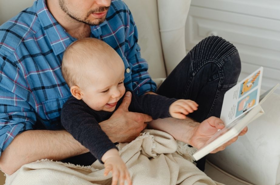 bebé interactuando con adulto mientras miran un libro de cartón