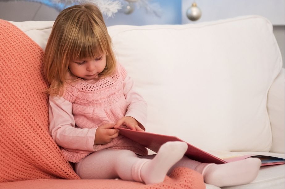 niña de 2 años leyendo un cuento sentada en el sofá