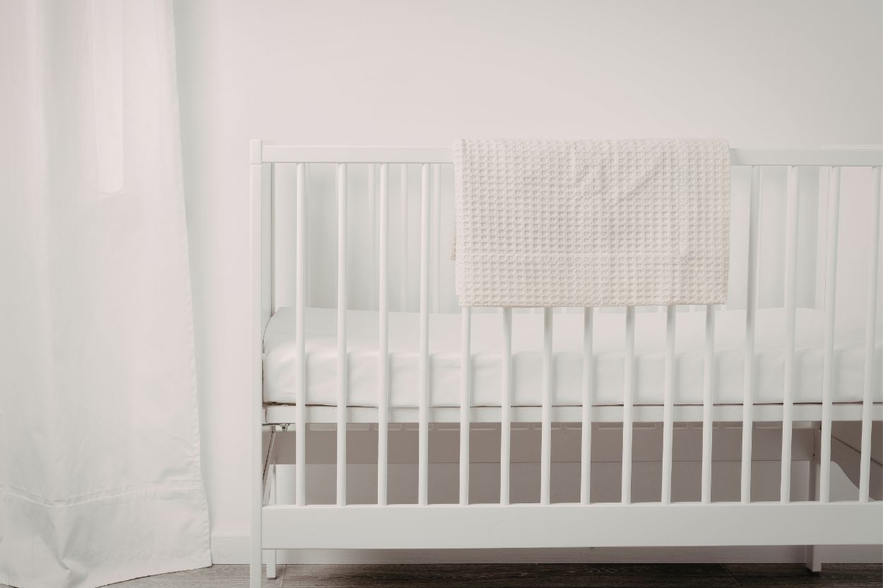 Cuna segura para recién nacido con barrotes blancos y colchón firme en un entorno tranquilo.