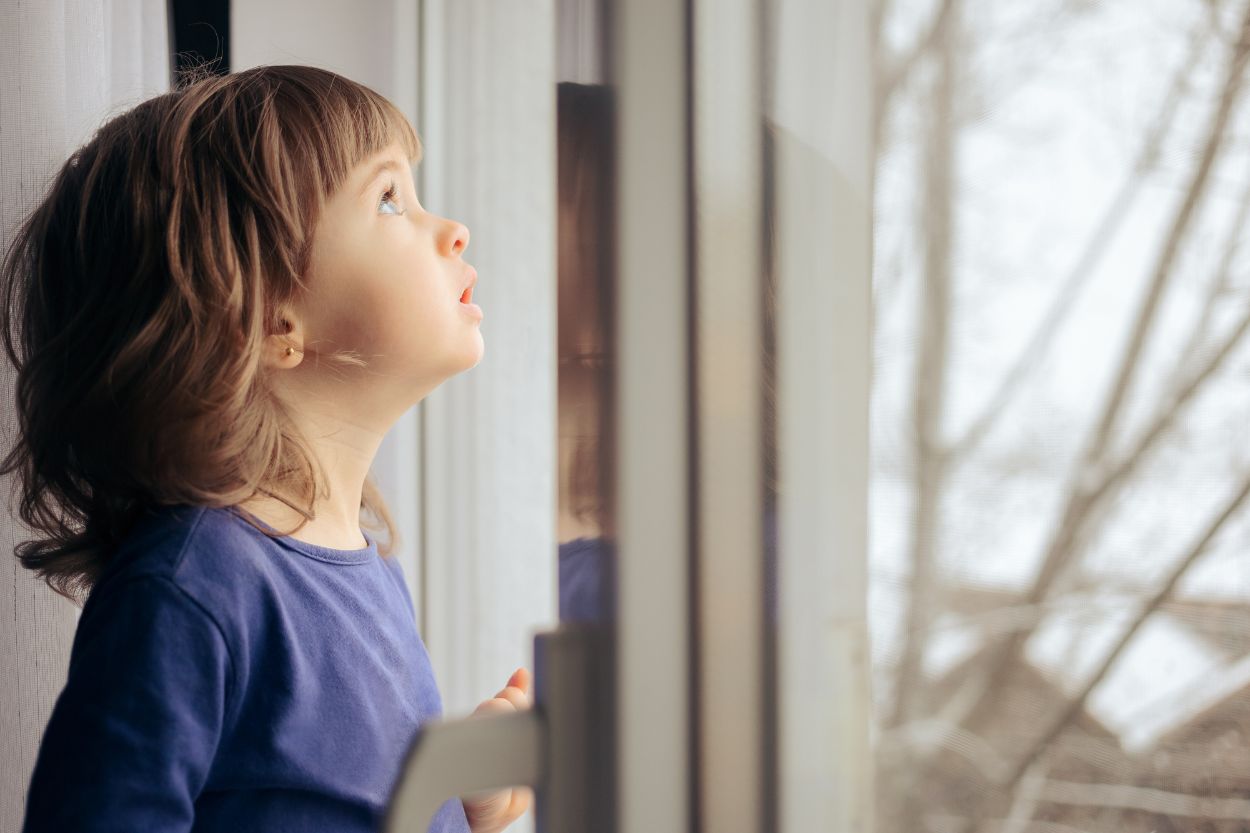 Niña pequeña observando por la ventana con gesto curioso