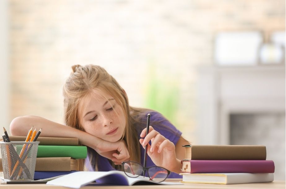 Niña de primaria apoyada sobre libros mostrando aburrimiento o desmotivación escolar en niños con altas capacidades.
