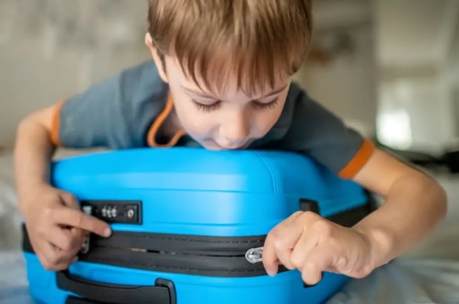 Niño cerrando una maleta para las vacaciones de verano con ropa infantil.