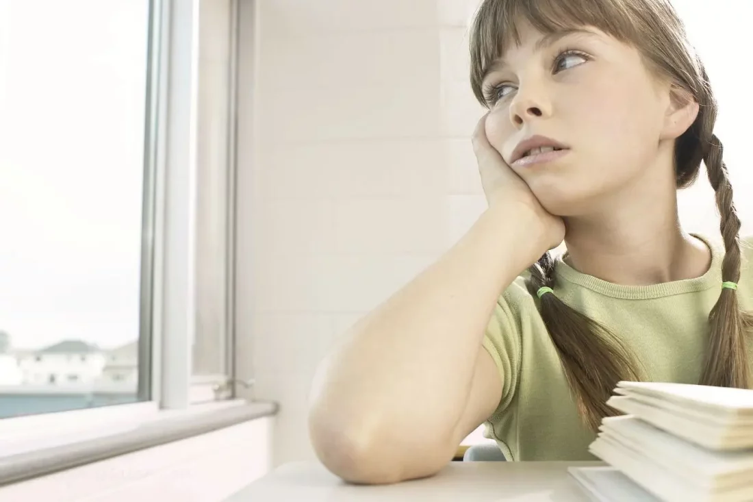 Niña aparentemente distraída en clase mirando por la ventana mientras piensa